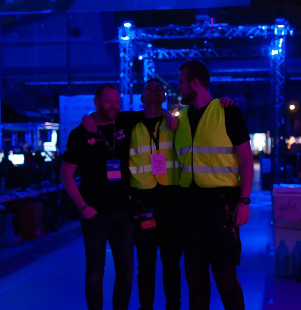 Tre crewmedlemmer med armene om hinanden i den blå belysning i hallen